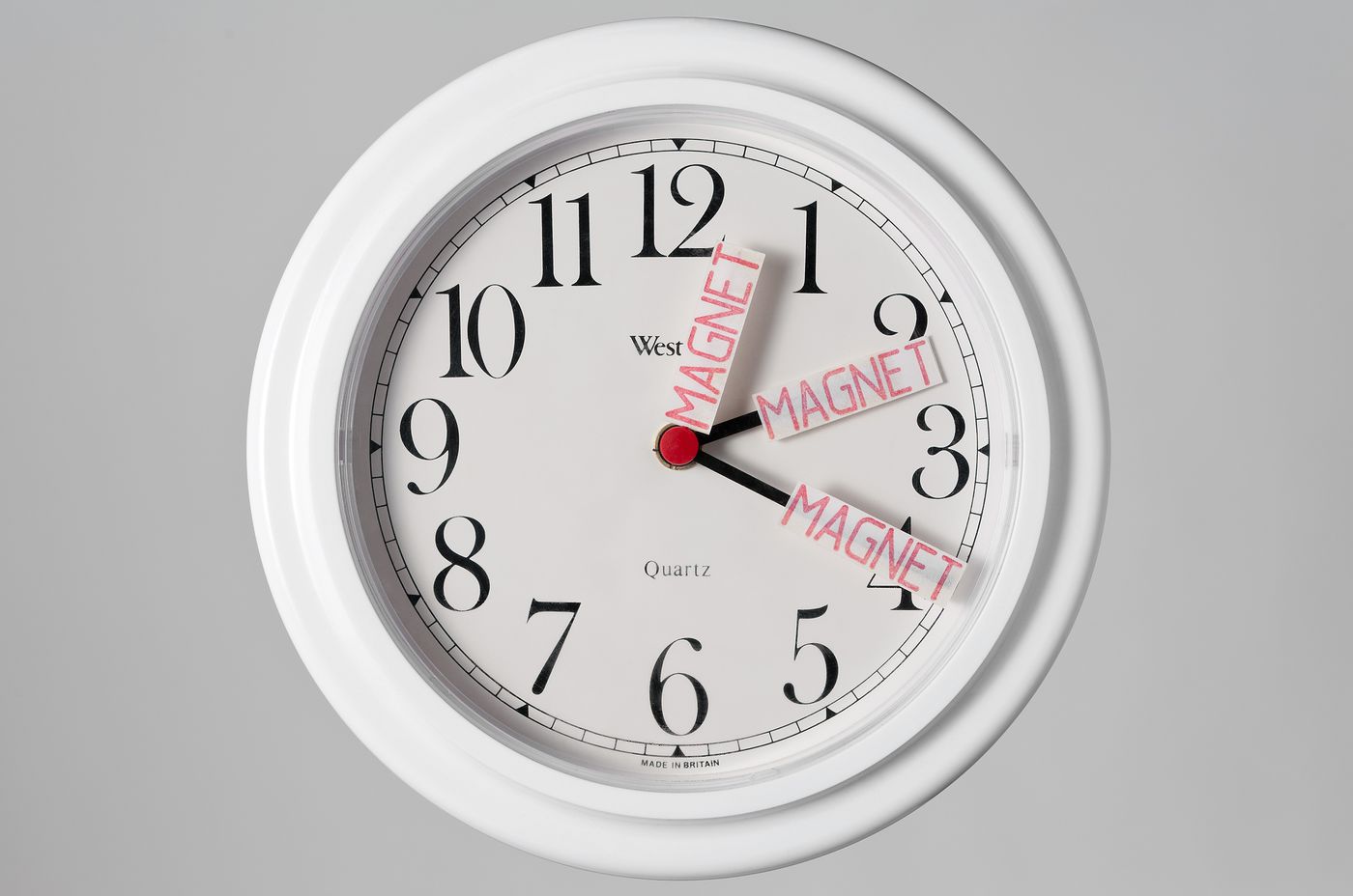 Quartz clock with slips of paper stamped "Magnet" attached to hands