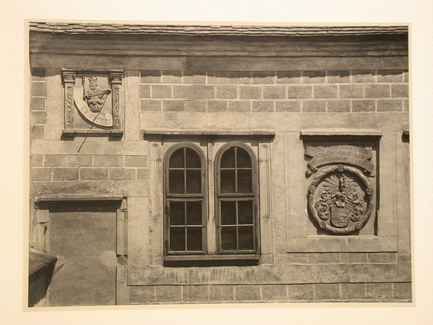 Close-up view of a window and panels with relief carvings showing figures, text and a coat of arms, possibly located in a courtyard of Telc Château, Telc, Czechoslovakia (now Czech Republic)