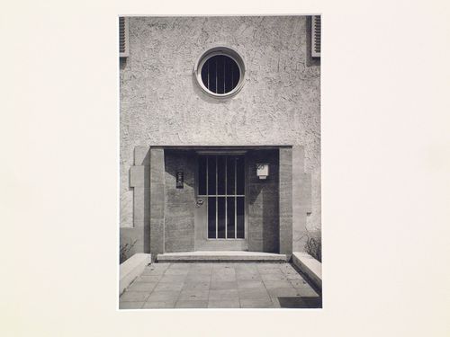 Detail, entrance to stucco house, with barred door, and round window above
