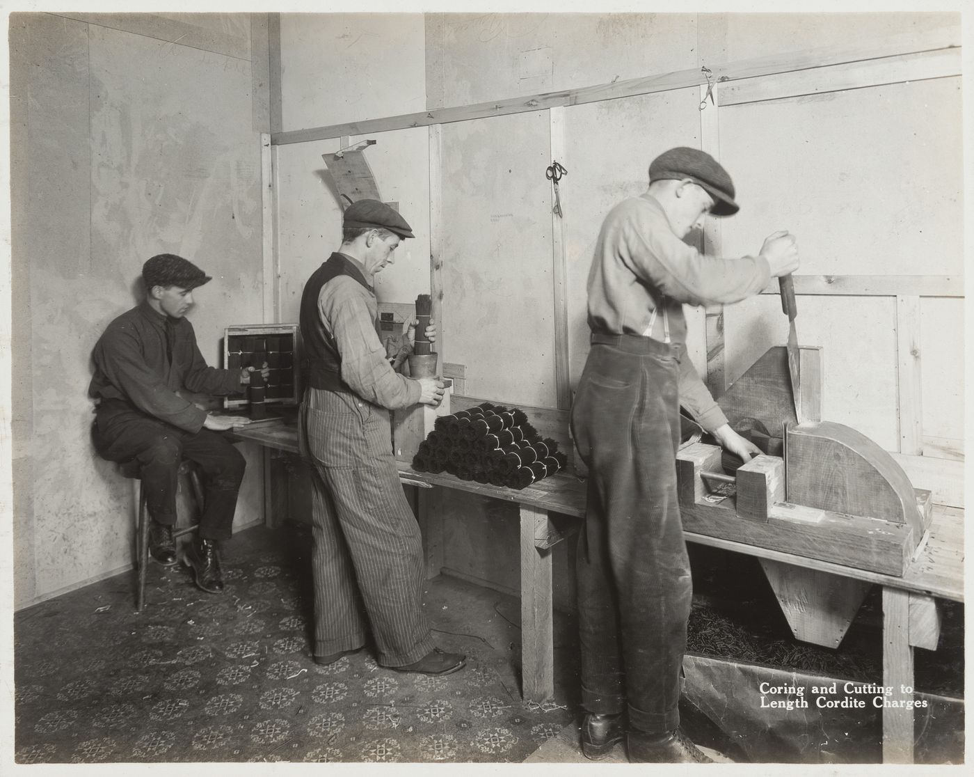 Interior view of workers coring and cutting to length cordite charges at the Energite Explosives Plant No. 3, the Shell Loading Plant, Renfrew, Ontario, Canada