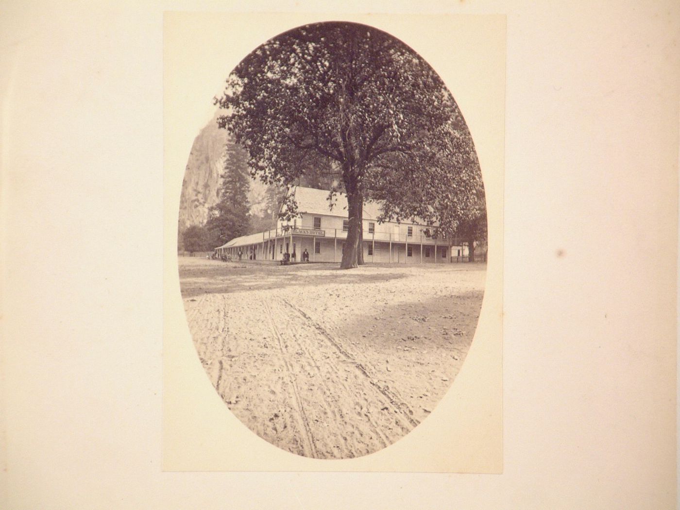 Road in foreground leading to Black's Hotel, two large trees, people out front, Yosemite Valley, California