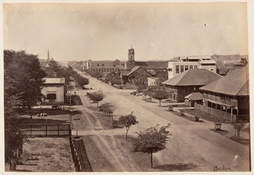 View of Merchant Street showing buildings, a clock tower and a church tower, possibly from the Roman Catholic Cathedral, in the left background, Rangoon (now Yangon), Burma (now Myanmar)