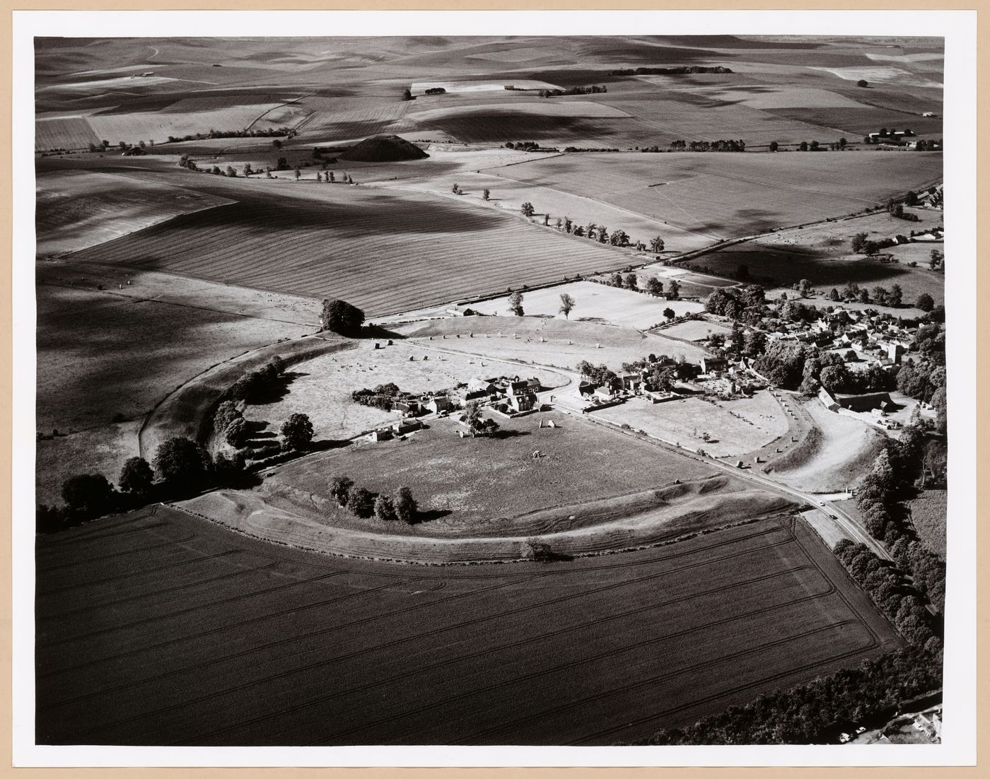 Partial aerial view of Avebury showing houses and roads enclosed by a henge and with Silbury Hill in the distance, Avebury, Wilthire, England