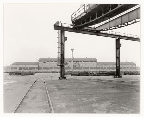 Partial view a bridge crane with a warehouse and lumber in the background, Marghera, Italy