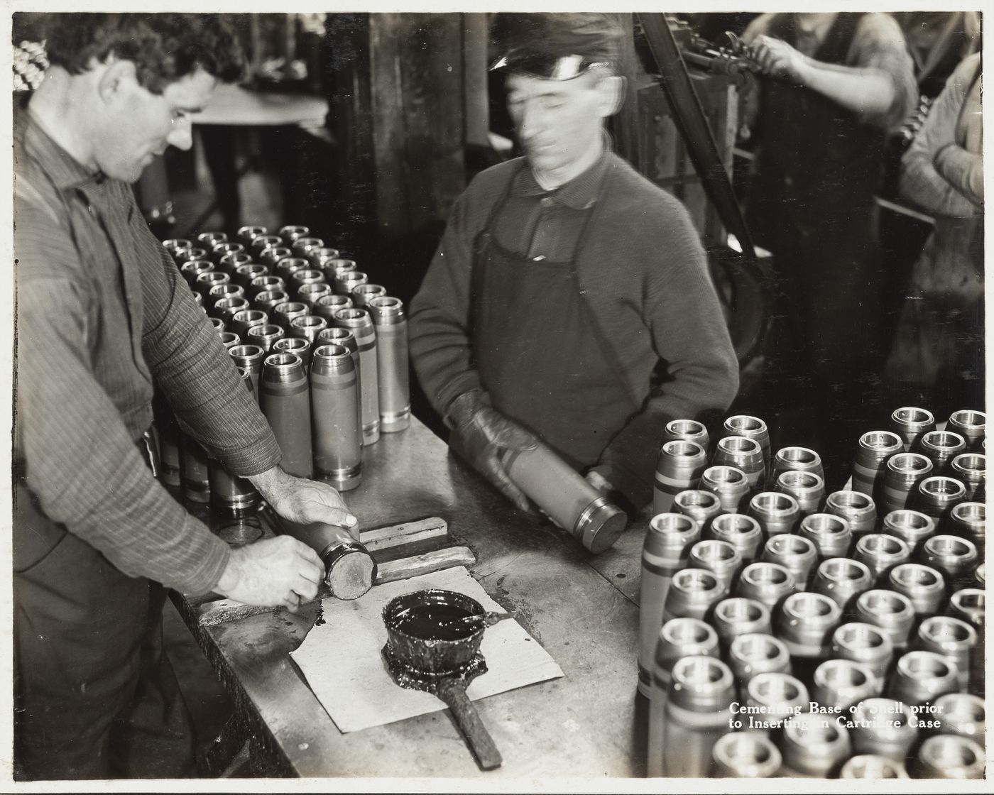 Interior view of workers cementing base of shell prior to inserting in cartridge case at the Energite Explosives Plant No. 3, the Shell Loading Plant, Renfrew, Ontario, Canada