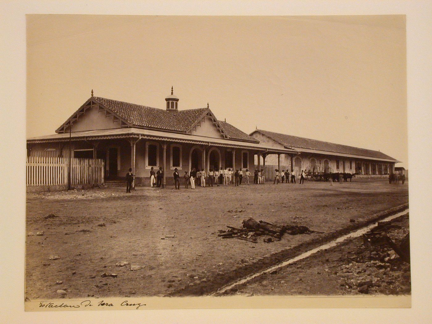 View of the principal façade of the Veracruz railway station with a gutter and rubbish in the foreground and men and horse-drawn vehicles in the background, Mexico