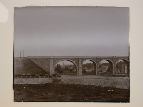 Partial view of a viaduct showing a town in the distance and railroad cars on the left, France ?