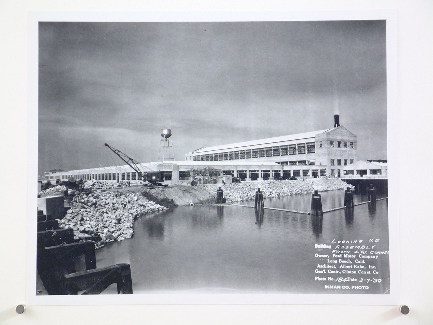 View of the south and east façades of the Assembly Building from the railroad bridge with a dock in the foreground under construction, Ford Motor Company Automobile Assembly Plant, Long Beach, California