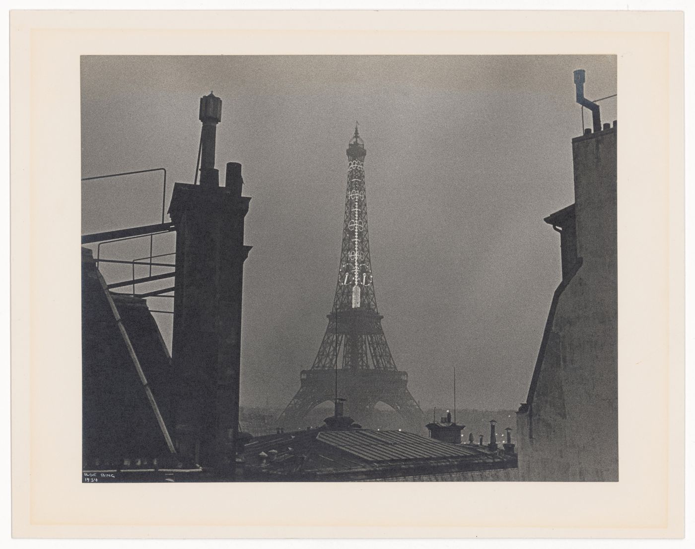 Eiffel Tower with lit thermometer, seen at night, bordered by building rooves (No. 6), Paris, France