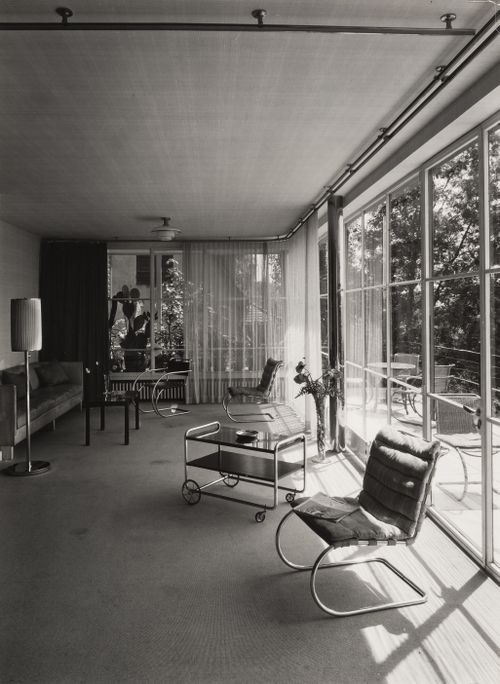 Interior, living room with tubular steel frame chairs and wheeled cart, patio visible beyond picture window