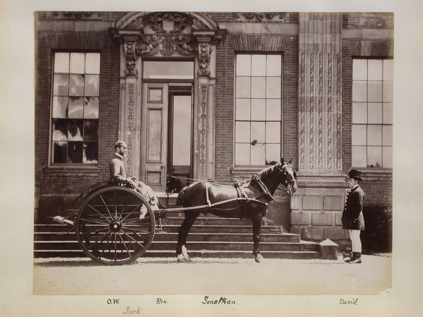 View of a gig with people and animals in front of a manor house, England