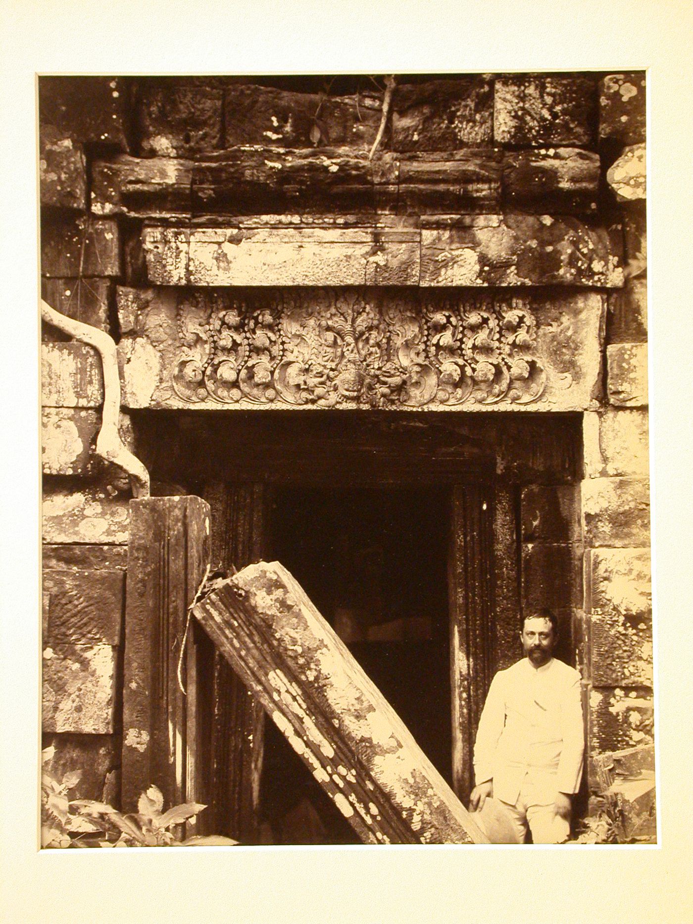 Portrait of a man standing beside the ruins of a temple, probably in Angkor, Siam (now in Cambodia)