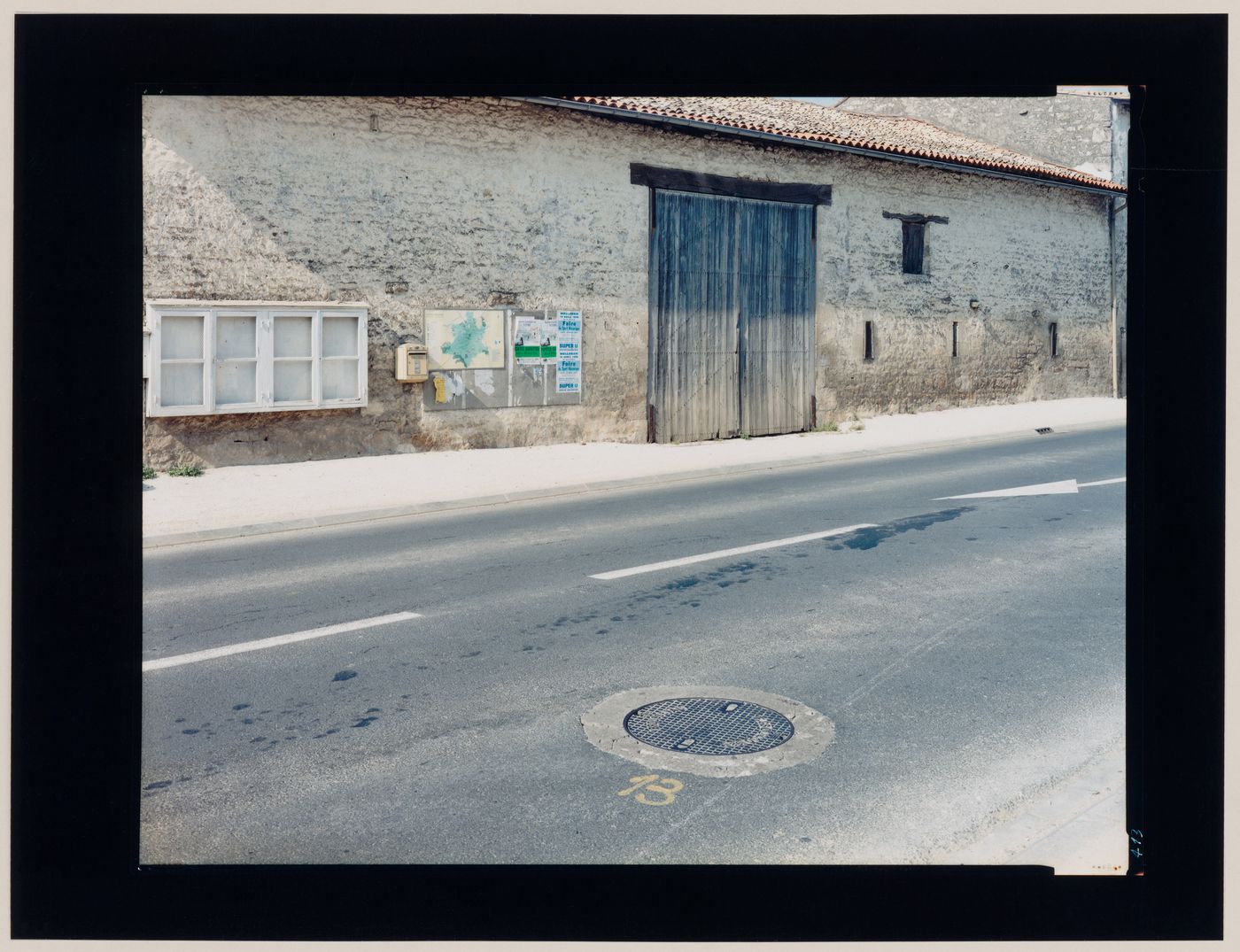 View of a stone building with wooden doors and a street, Dax, France (from the series "In between cities")
