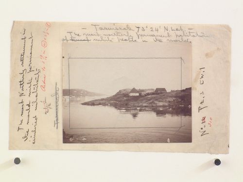 Distant view of houses, dock and figures on rocksby the water, Tasuissak, Greenland