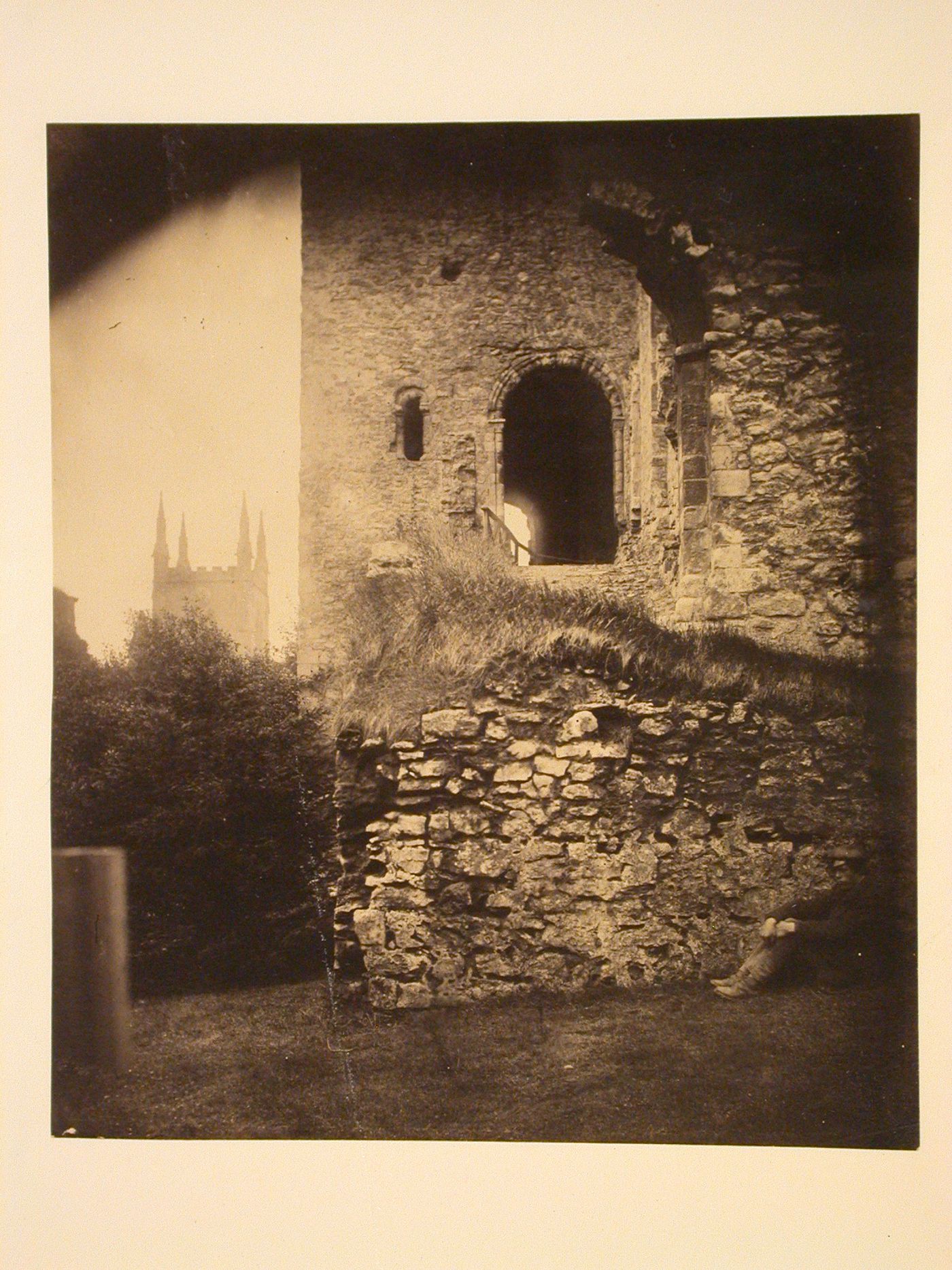 Man seated near stone wall and tower, England ?