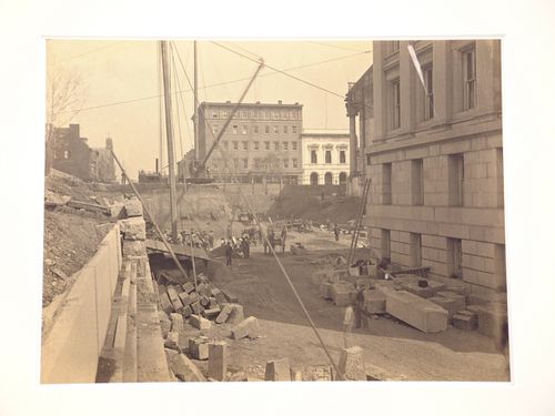 Treasury Building under construction: View of ground level work crews, crane, worker and stone blocks on ground, Washington, District of Columbia