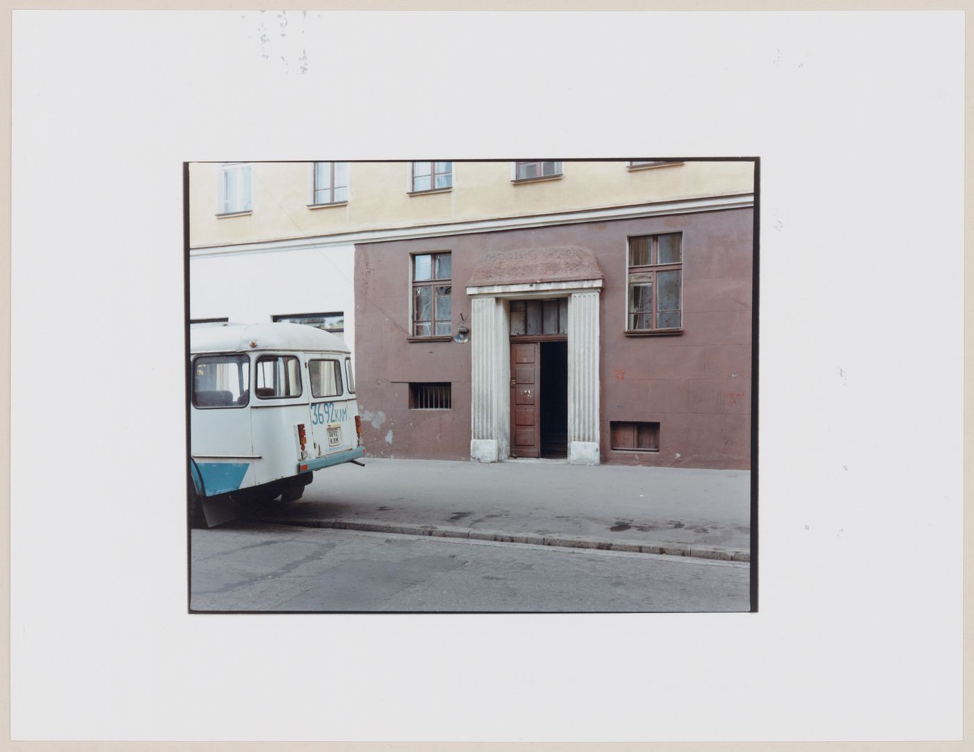 View of an apartment house showing a doorway, a street, and a parked bus, Kaliningrad, Kaliningradskaia oblast', Russia (from the series "In between cities")