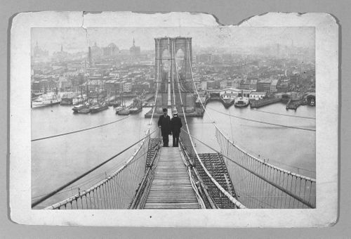 View of two men standing on end of completed section of Brooklyn Bridge, New York City, New York