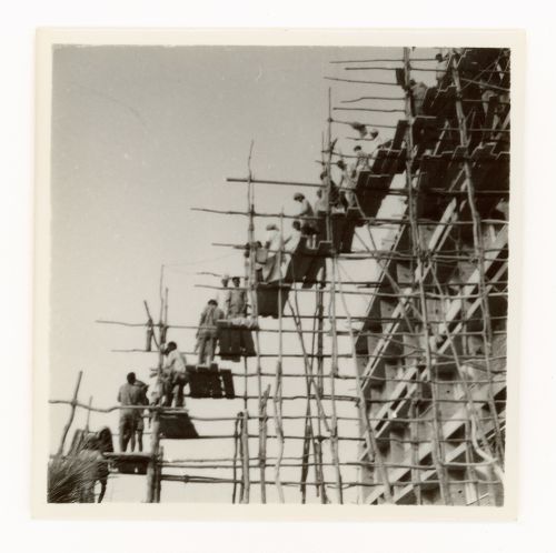 View of construction workers on wooden scaffolding passing on material supplies to upper levels of building, Chandigarh, India