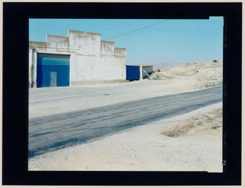 View of an agricultural building showing a concrete wall, a metal door, a road and hills, Castrojeriz, Burgos Province, Spain (from the series "In between cities")