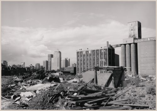 Field Work in Montreal: View of a wooden shack-like structure, a dump and a grain elevator showing office towers in the background, Montréal, Québec