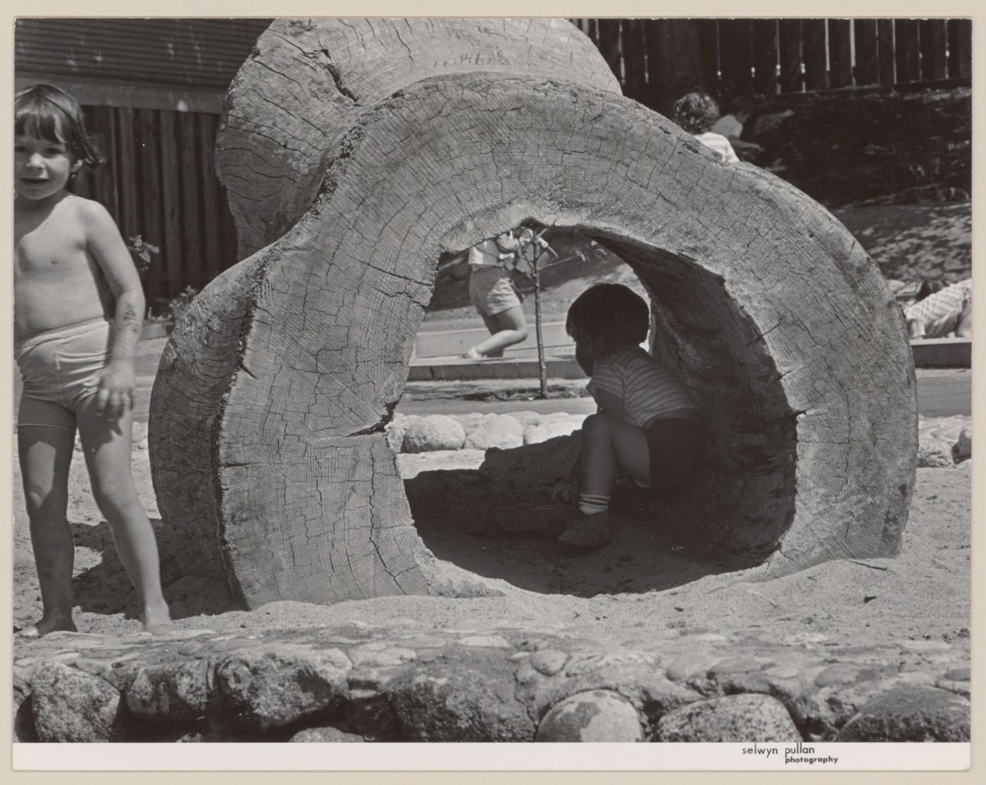 View children playing in hollow log from North Shore Neighbourhood House Playground, Vancouver, British Columbia