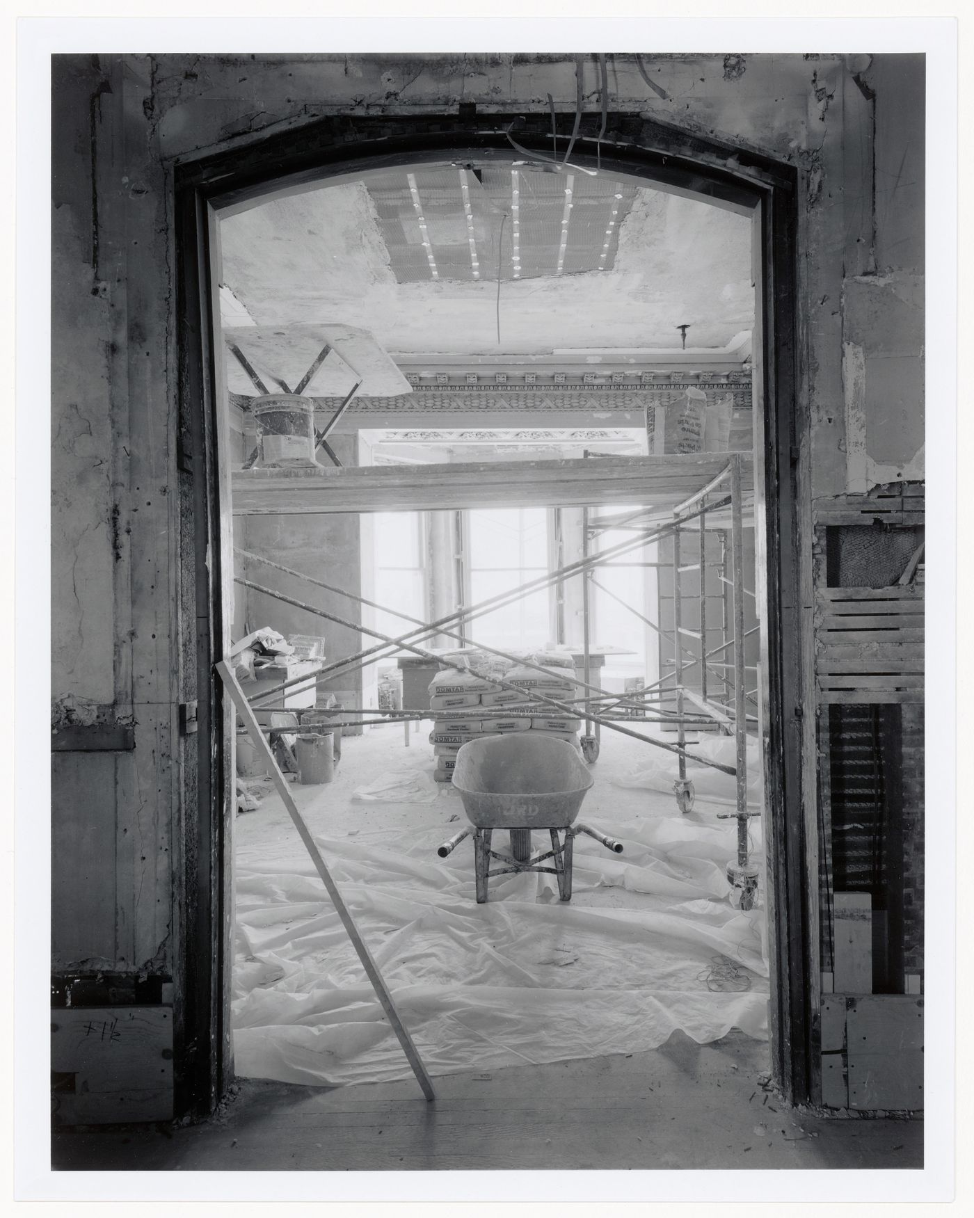 Interior view of the reception rooms showing scaffolds and a wheelbarrow in the foreground and a bay window in the background, Shaughnessy House under renovation, Montréal, Québec