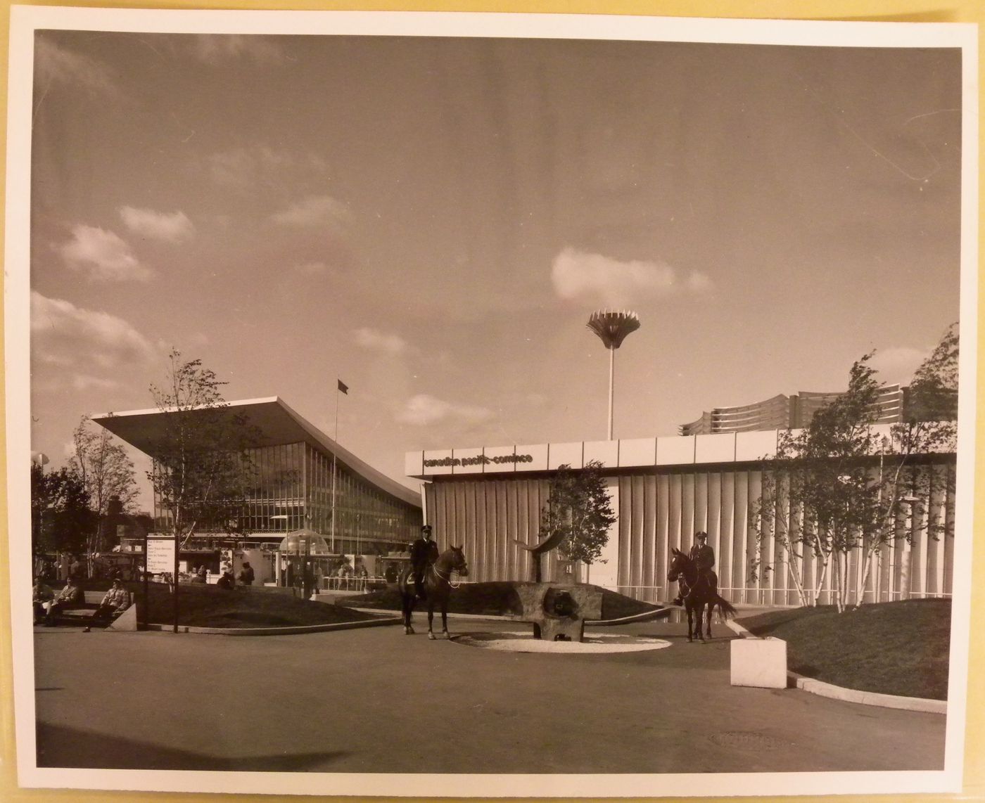 Two horsemen surrounding the sculpture "Polypède" by Charles Daudelin with the Canadian Pacific-Cominco Pavilion and the Pavilion of Soviet Union in background, Expo 67, Montréal, Québec