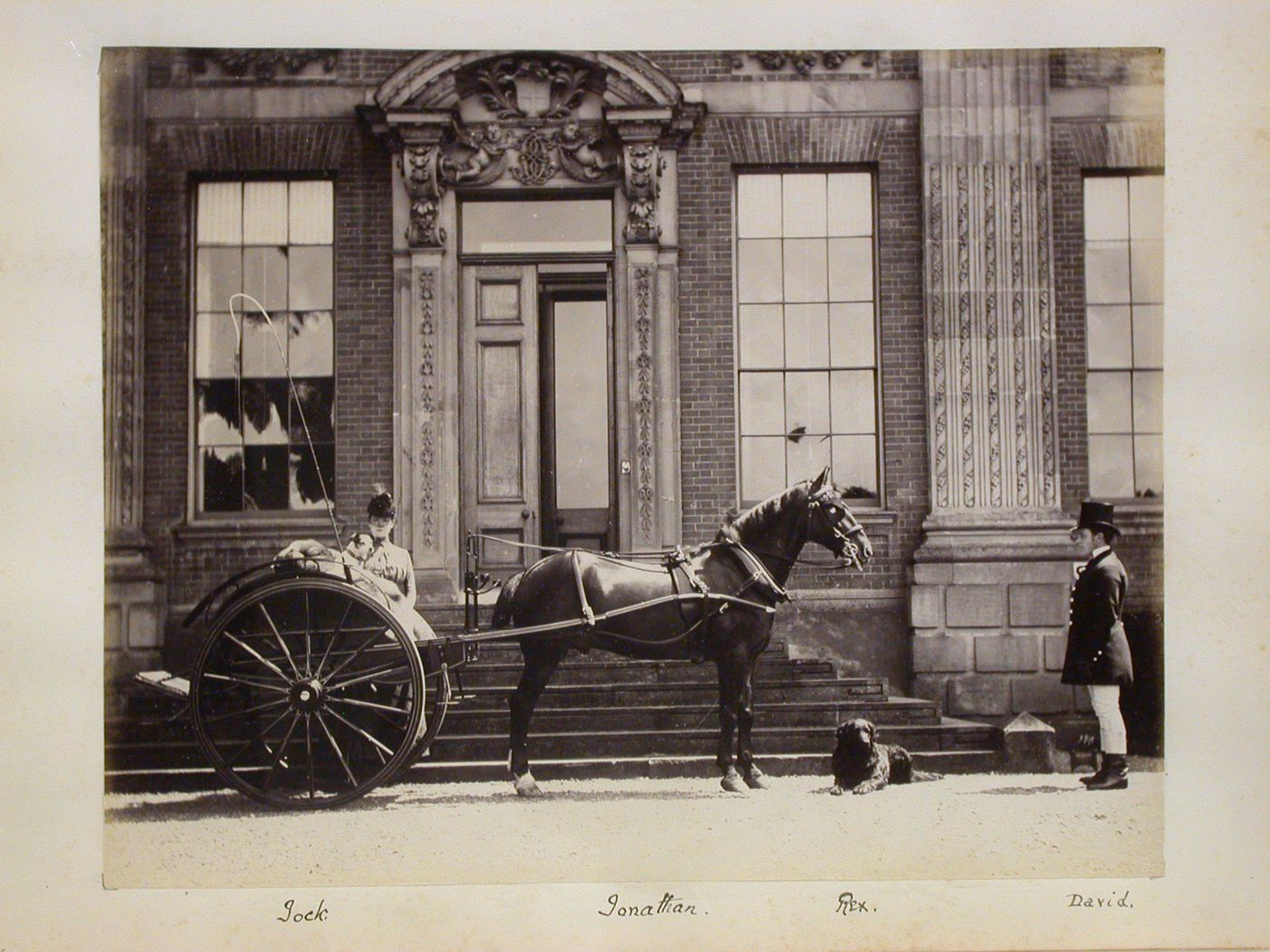 View of a gig with people and animals in front of a manor house, England