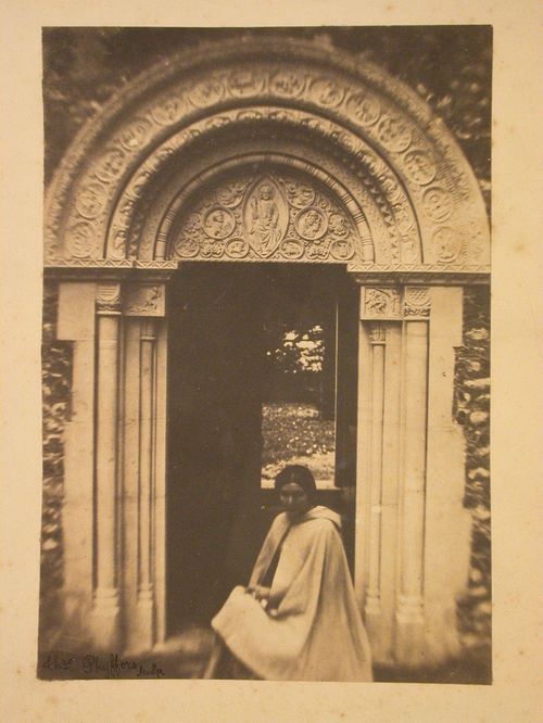 View of a woman standing in front of an ornamental doorway of a church [?], England [?]