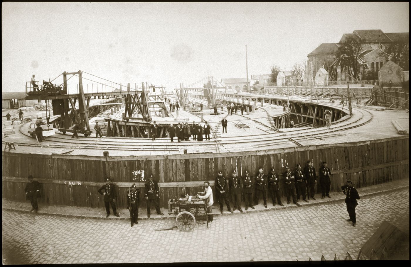 View of Sacré-Coeur construction site, enclosed by fence, with 13 men in uniforms standing outside, Paris, France