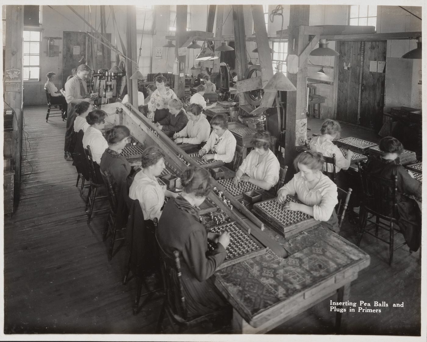 Interior view of workers inserting pea balls and plugs in primers at the Energite Explosives Plant No. 3, the Shell Loading Plant, Renfrew, Ontario, Canada