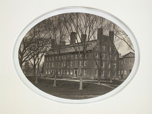 Exterior view of a college building with lawn and trees, figures in doorways, Harvard, Cambridge, Massachusetts