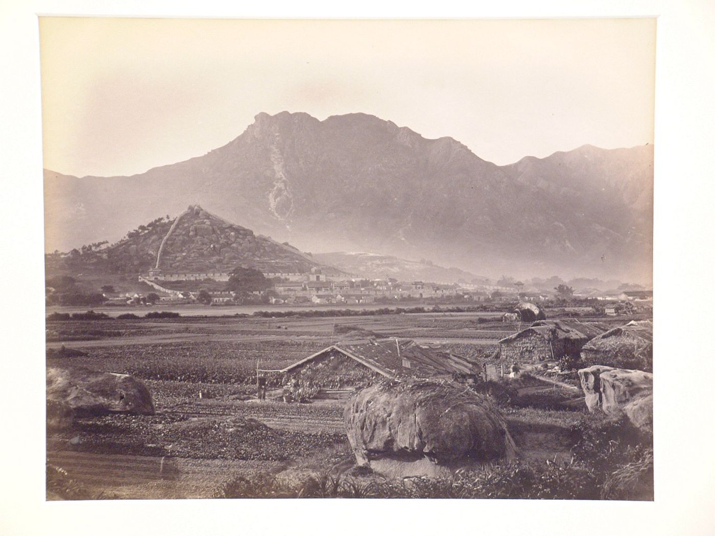 View of huts and agricultural land with the Kowloon Walled City in the background, Kowloon, Hong Kong (now Hong Kong, China)