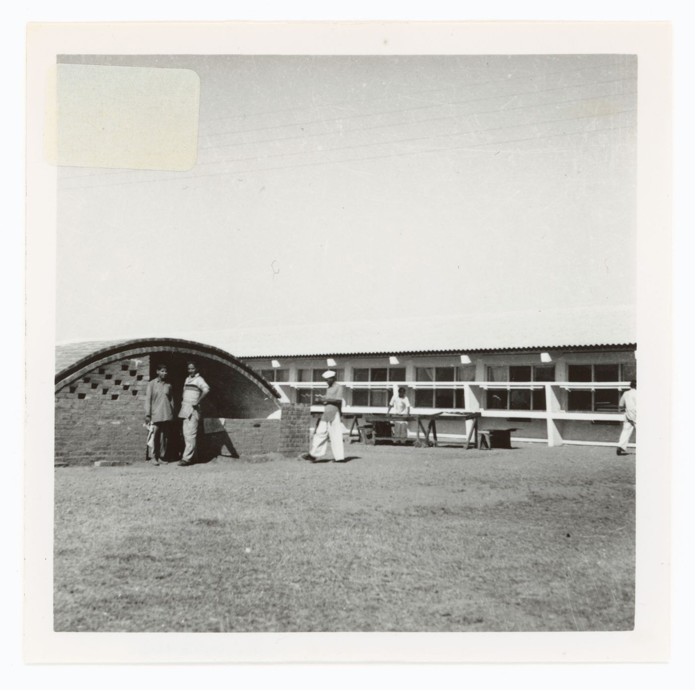 View of a barrel roof building under construction and workers with an unidentified building in background, possibly in Chandigarh, India