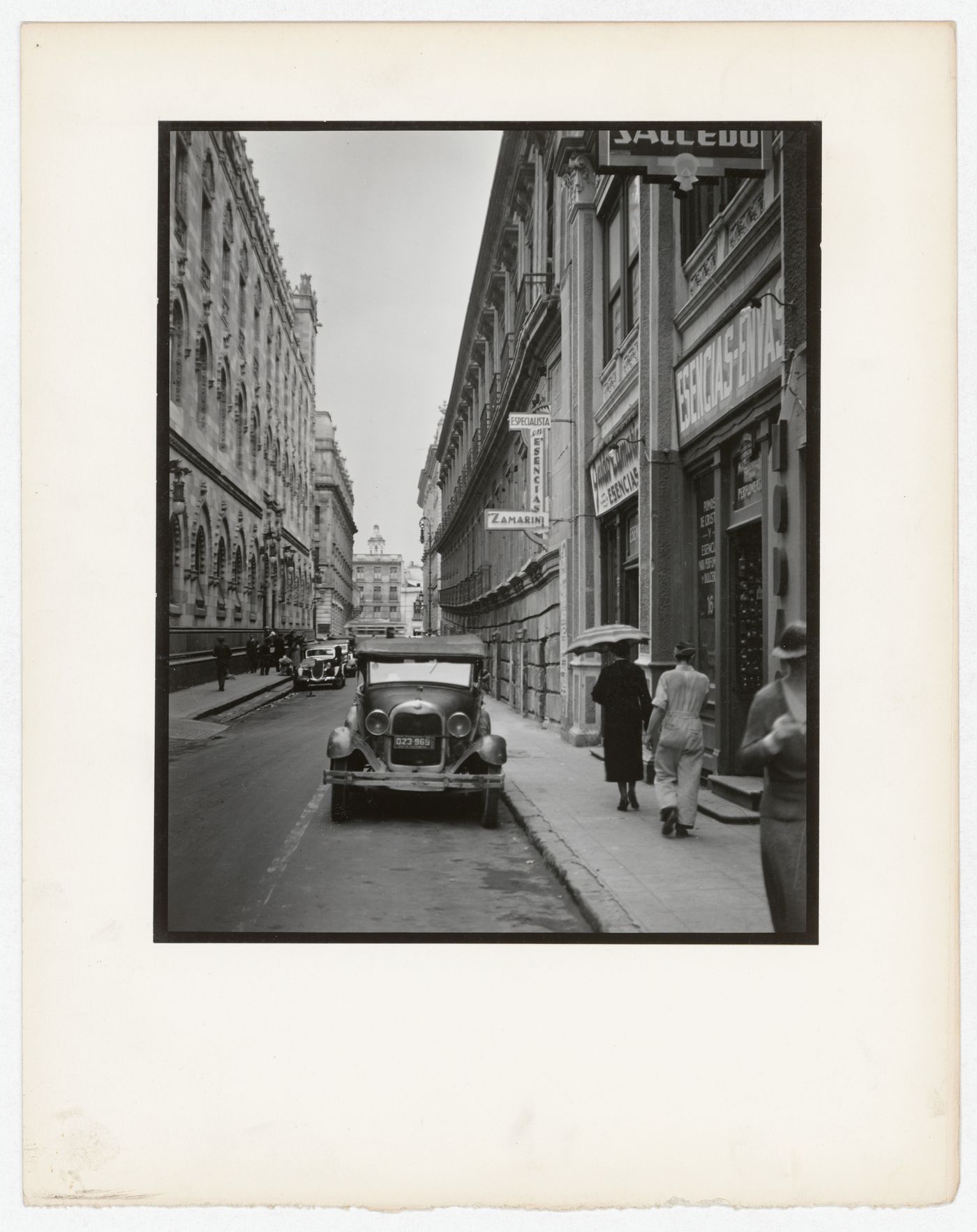 View of a street and buildings, one of which is possibly known as the School of Mines, with an automobile in the foreground, Mexico City, Mexico