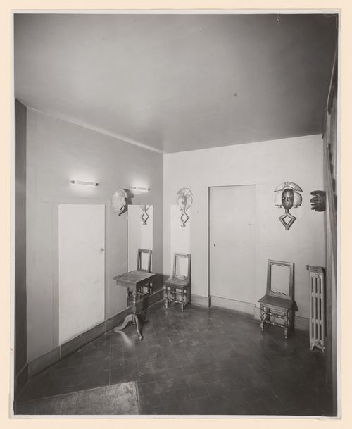 Corner of room with African [?] sculptures hung very high on the walls