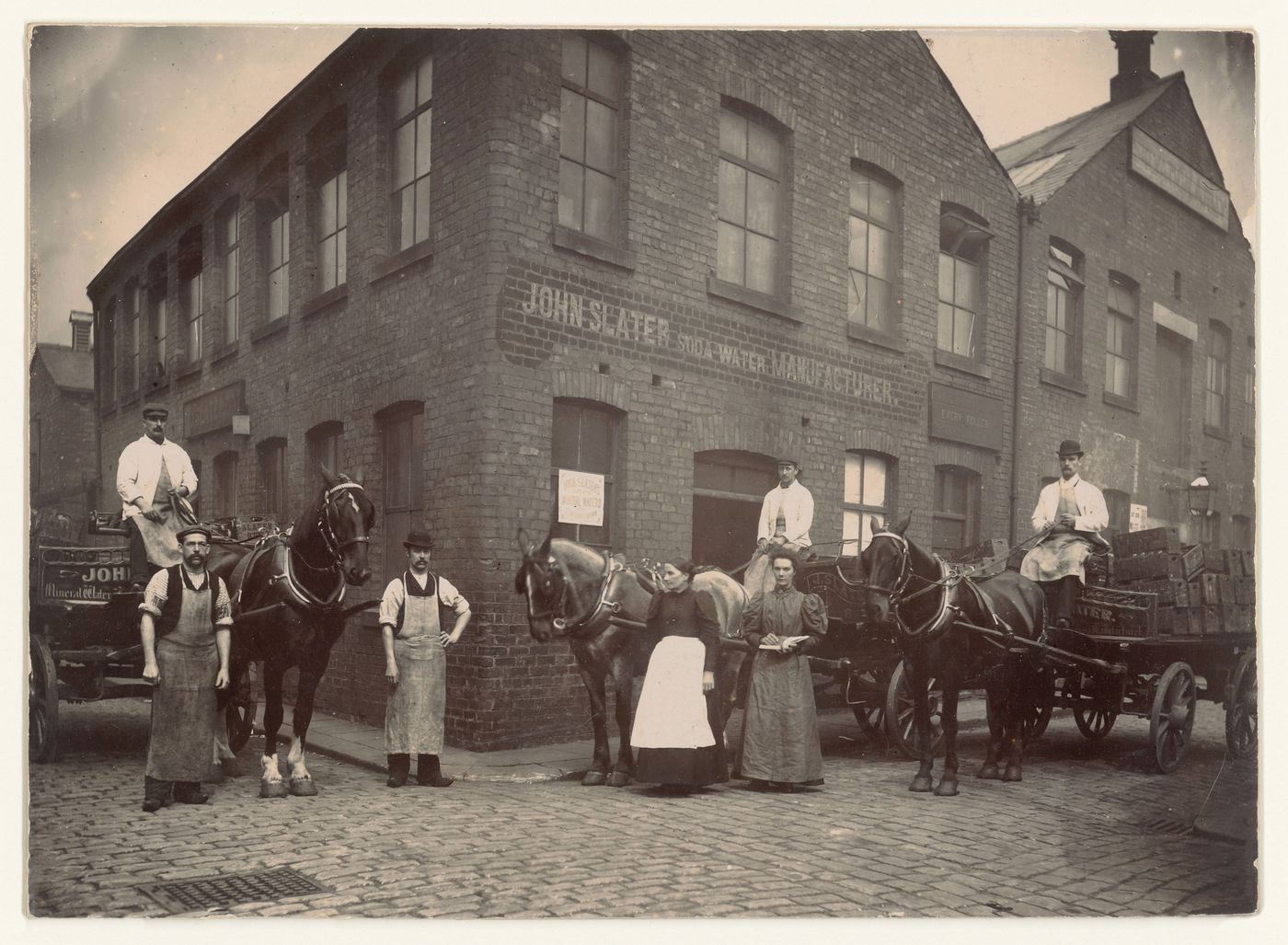 Men and women and delivery wagons in front of the John Slater Soda Water Manufacturing plant, Manchester, England