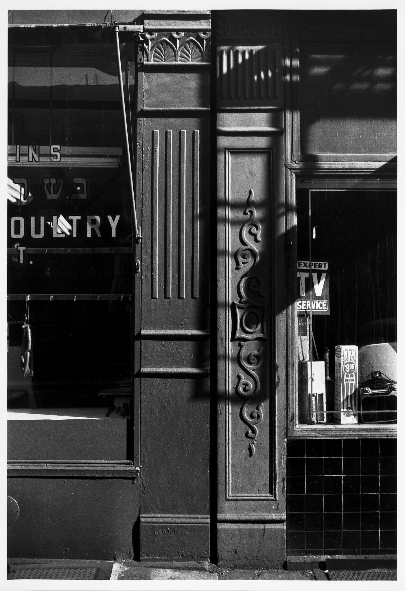 Partial view of two shop façades showing windows, two ornamented columns and the shadow of a fire escape, New York City, New York