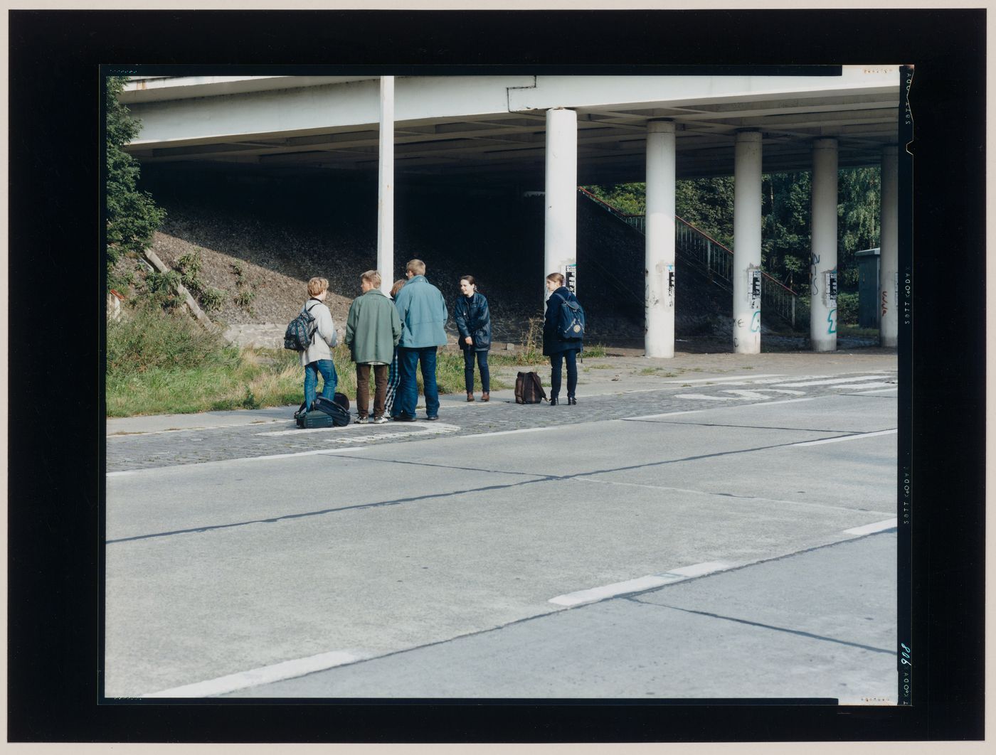 Group portrait of young people standing on the shoulder of a roadway showing the roadside under an overpass and columns, Jülich, Germany (from the series "In between cities")