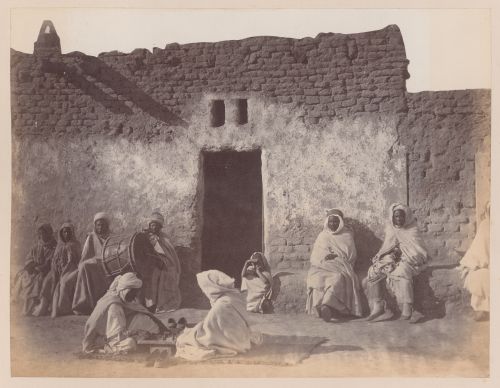 View of people with drum and board game sitting in front of adobe structure, Algiers, Algeria
