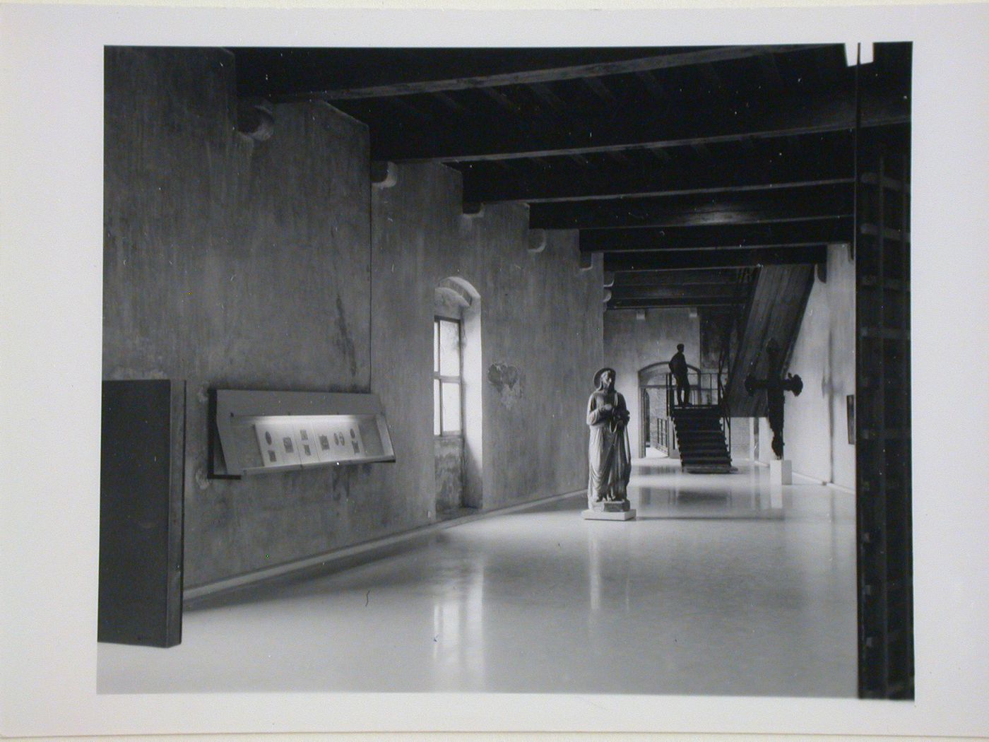 Interior view of a gallery showing a display case, statue, freestanding painted crucifix and a staircase, Museo di Castelvecchio, Verona, Italy