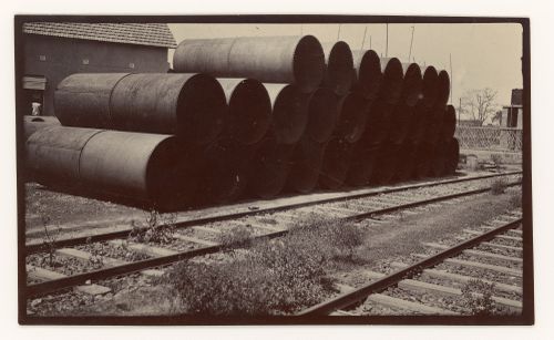 View of riveted pipes stacked next to train tracks, unknown location