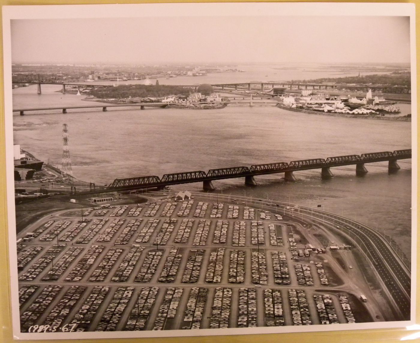 Aerial view of the Île Notre-Dame and Île Sainte-Hélène sites with Victoria Bridge and the Victoria Autopark in foreground, Expo 67, Montréal, Québec