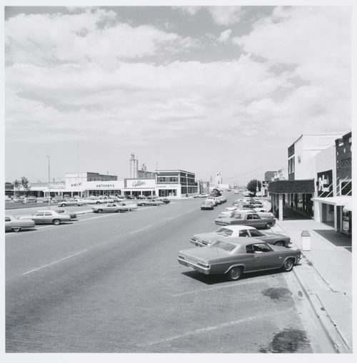 Town streets with cars, grain elevator in background, Brownfield, Texas