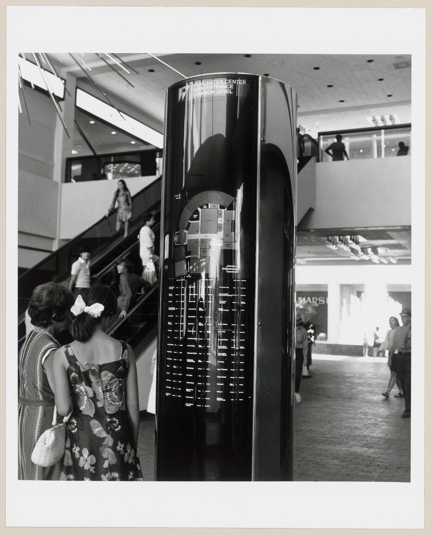 Interior view of the shopping mall at Worcester Center showing a guidepost bearing a floor plan, escalators, a mezzanine and people, Worcester, Massachusetts