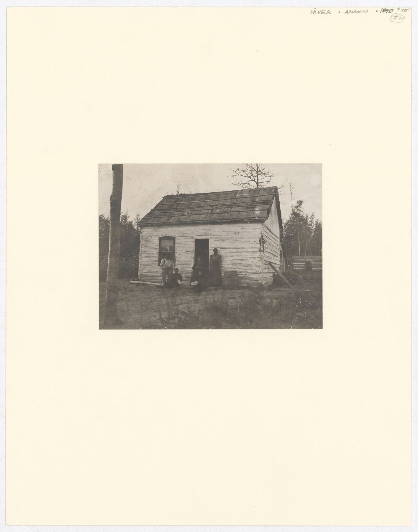 View of family in front of log cabin, probably North America