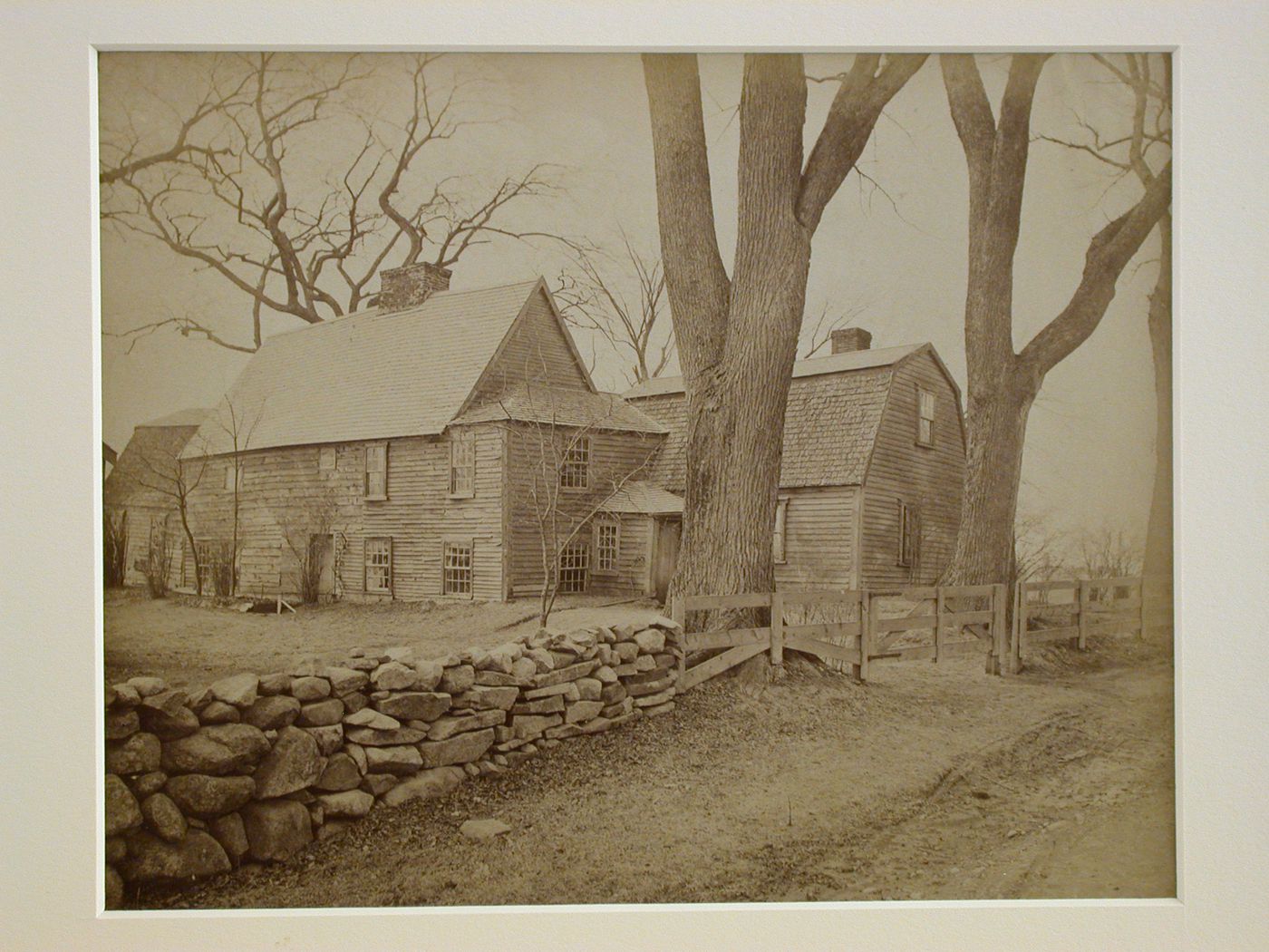 Side view from road of wooden house, stone and wooden fences bordering yard, United States