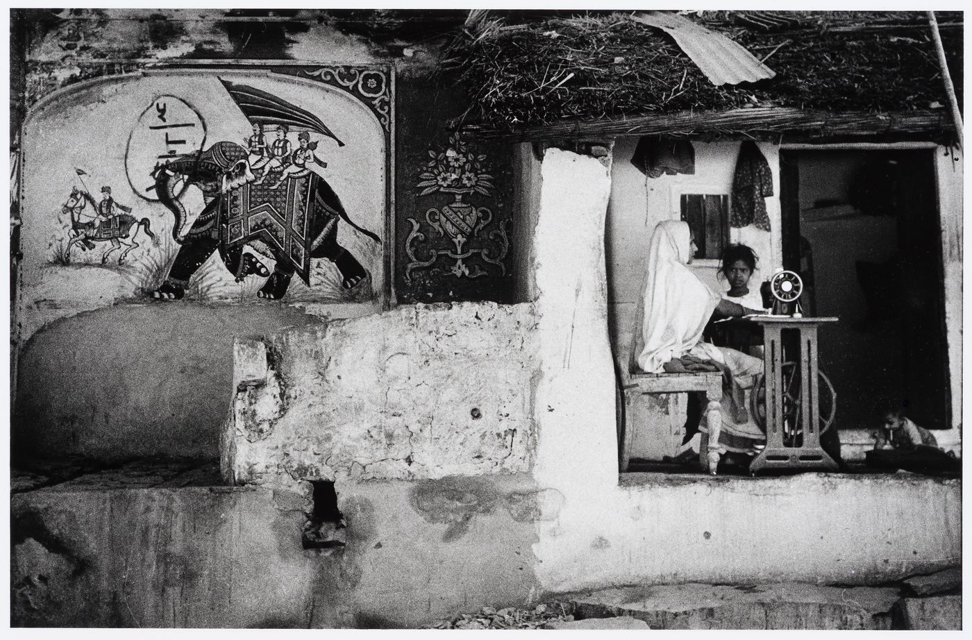 Partial view of a façade of an unidentified building showing a mural and a woman sewing, Jaipur, India
