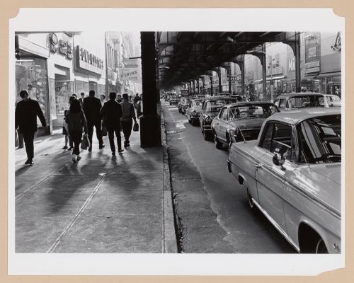 View of Jamaica Avenue showing people walking on the sidewalk and cars stopped in a traffic jam under an elevated subway line, Long Island, United States